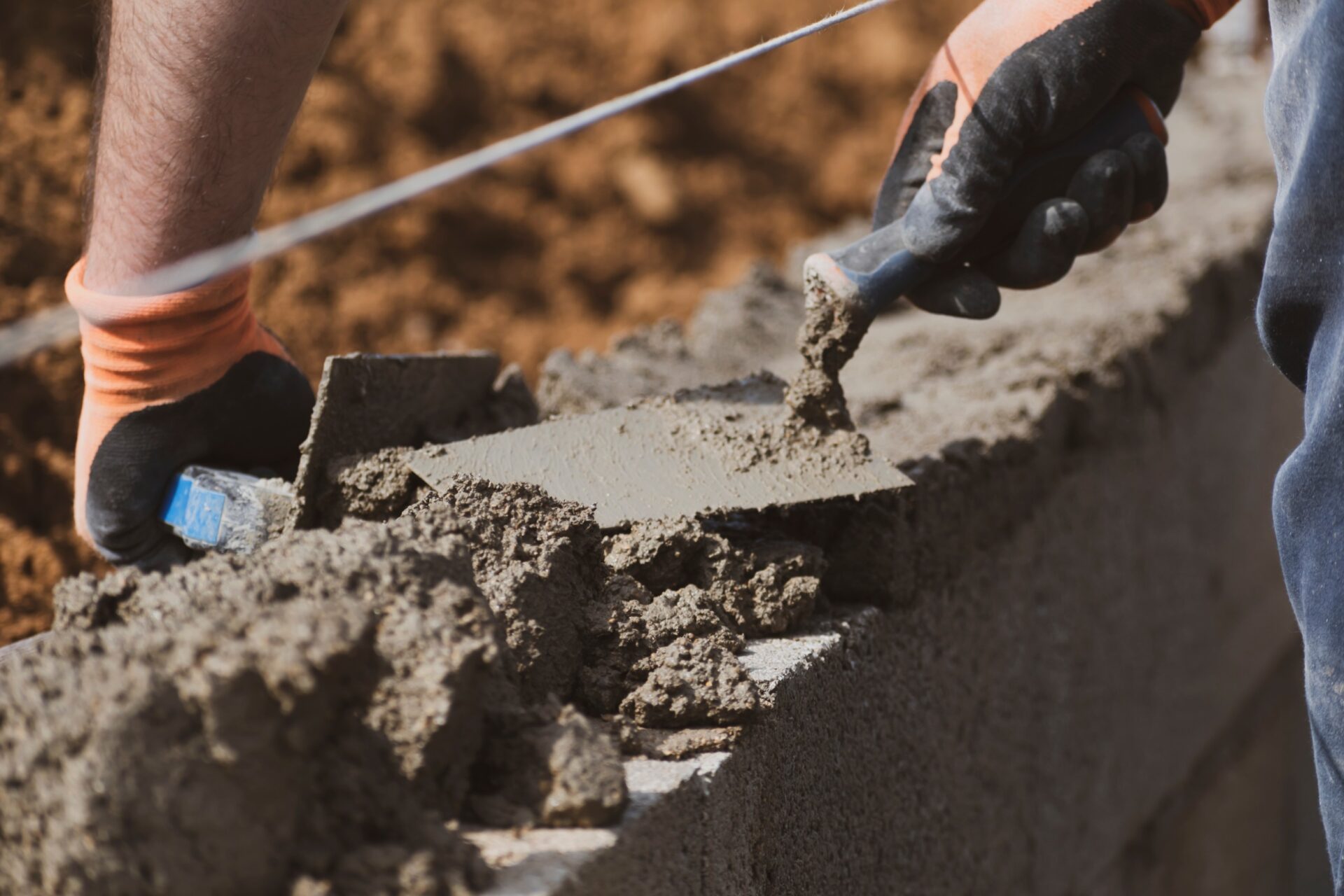 Bricklayer in glove spreading concrete to build a wall on construction site