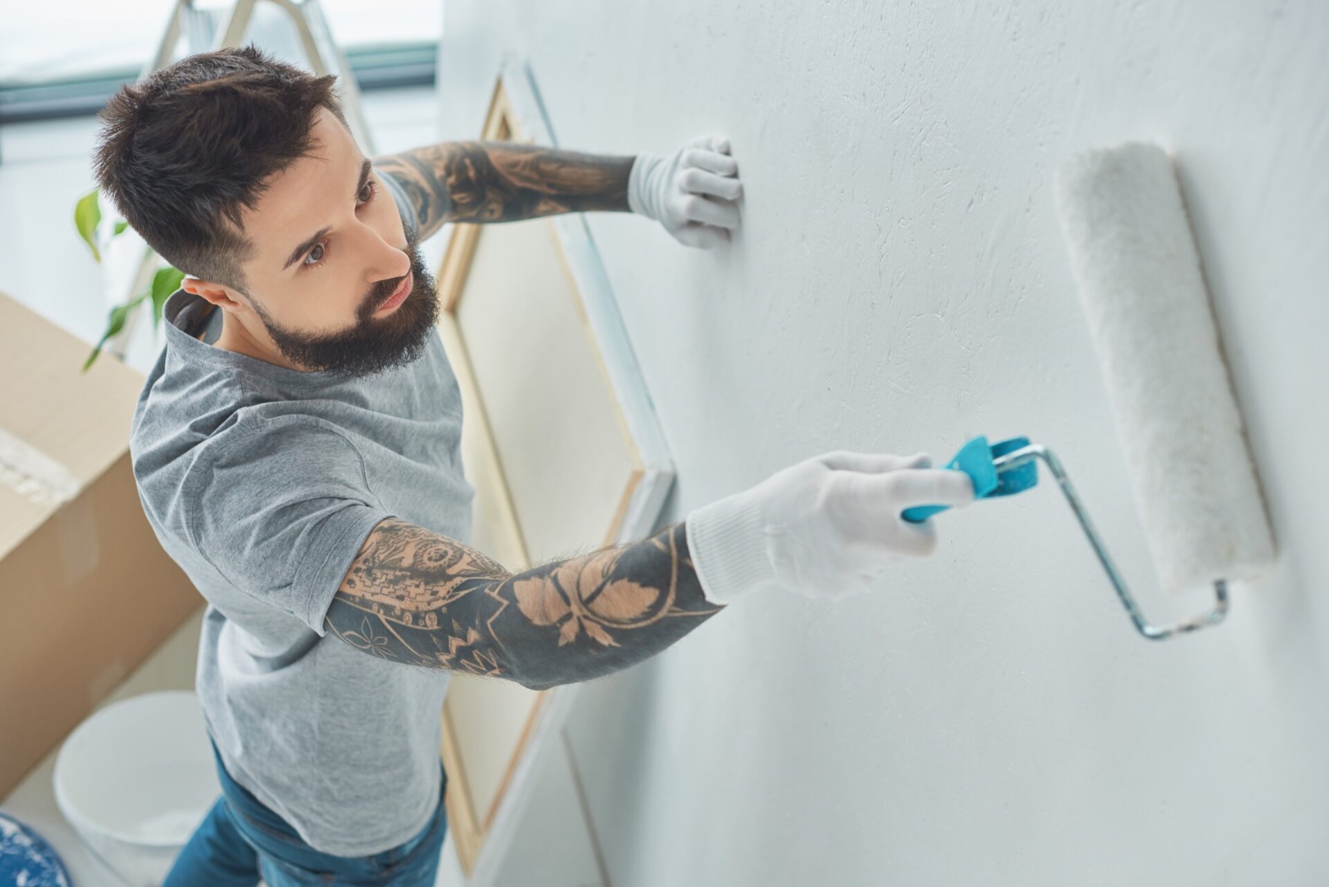 Side view of tattooed repairman painting wall in new apartment